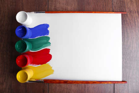 Colorful paint strokes with brush and paint cans on white sheet of paper on wooden table backgroundの写真素材