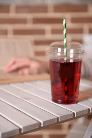 Pomegranate juice in fast food closed cup with tube on wooden table and female hand on brick wall backgroundの写真素材