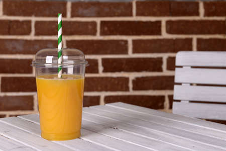 Orange juice in fast food closed cup with tube on wooden table and brick wall backgroundの写真素材