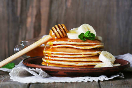 Stack of pancakes with mint, honey and slices of banana on rustic wooden backgroundの写真素材