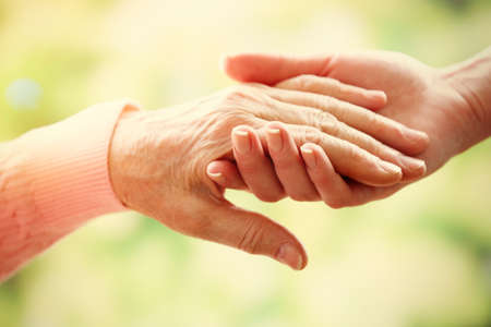 Old and young holding hands on light background, closeup