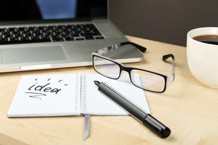 Cup of coffee with note Idea in notebook and glasses on wooden table and dark backgroundの写真素材