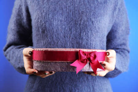Gift box in female hand on color backgroundの写真素材