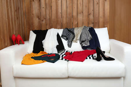 Messy clothing with shoes on white sofa, on wooden planks  backgroundの写真素材