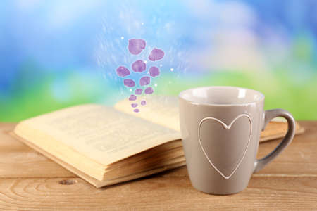 Open book with flying petals on table on bright backgroundの写真素材