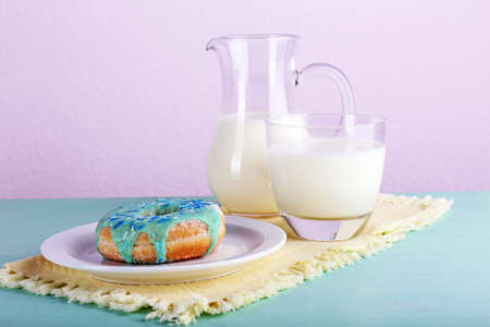 Glazed donut with glass and jug of milk on wooden table with napkin and color white planks backgroundの写真素材
