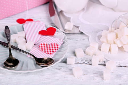 Heart shaped teabag tags, spoon and sugar cubes on saucer on wooden backgroundの写真素材