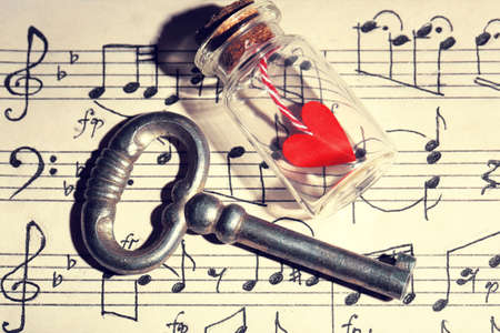 Retro key with heart in small glass bottle on music book backgroundの写真素材