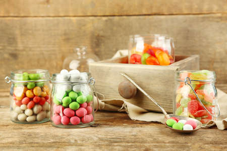 Multicolor candies in glass jars on wooden background