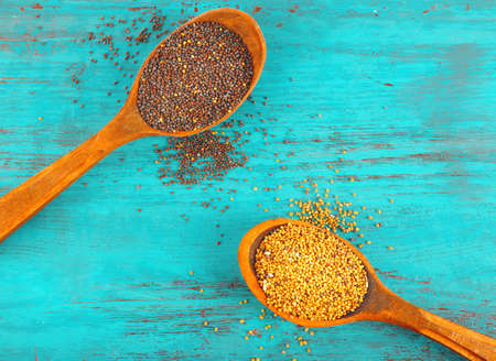 Two kinds of mustard seeds in wooden spoon on color wooden table backgroundの写真素材