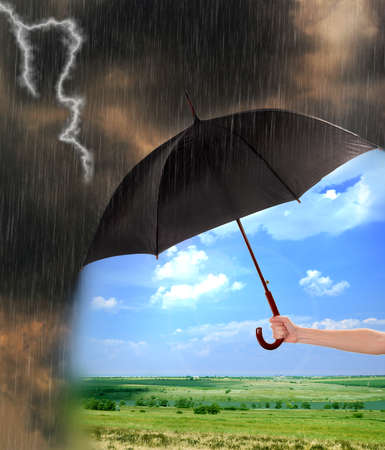 Black umbrella in hand protecting good weather from dark clouds of rainの写真素材