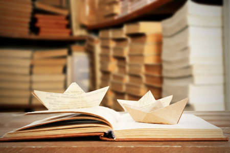Open book with paper boats on bookshelves backgroundの写真素材