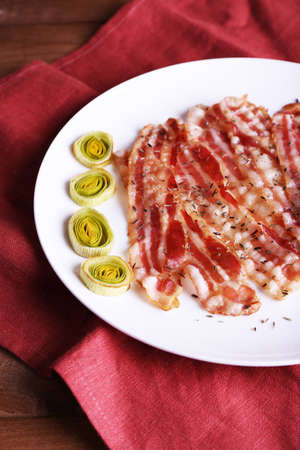 Strips of bacon with slices shallot in white plate with napkin on wooden table backgroundの写真素材