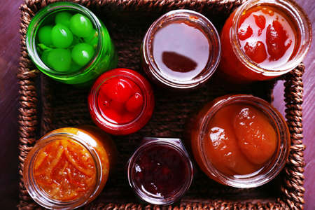 Homemade jars of fruits jam in wicker basket and color wooden backgroundの写真素材