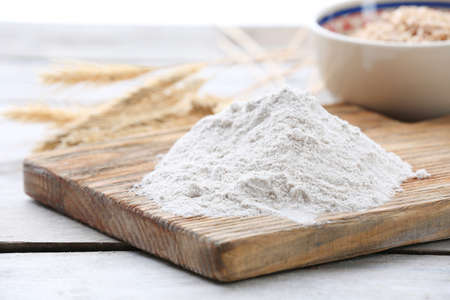 Heap of flour on cutting board with ears and grains in bowl on wooden tableの写真素材