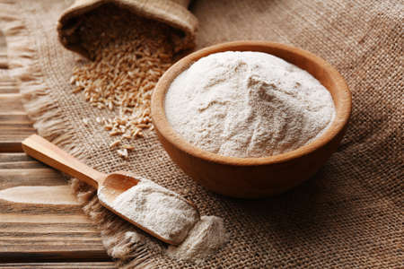 Flour in bowl with grains in bag on sackcloth backgroundの写真素材