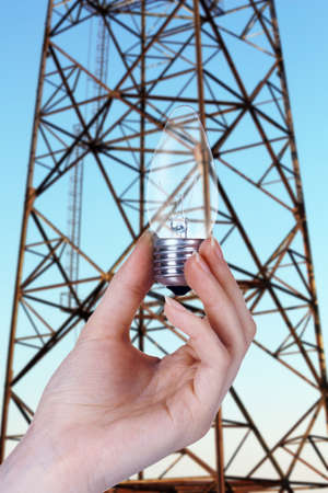 Light bulb in hand on high voltage line backgroundの写真素材