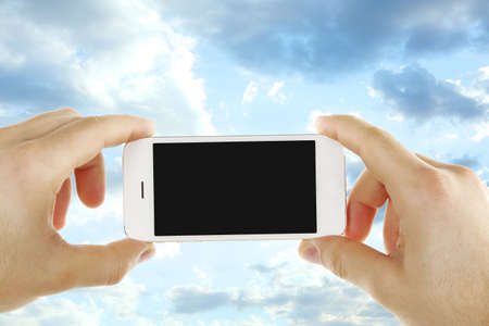 Hands holding mobile smart phone on sky backgroundの写真素材