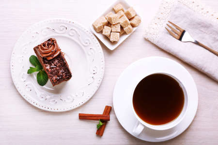 Tasty piece of chocolate cake with mint and cinnamon near cup of tea and lump sugar on wooden table backgroundの写真素材
