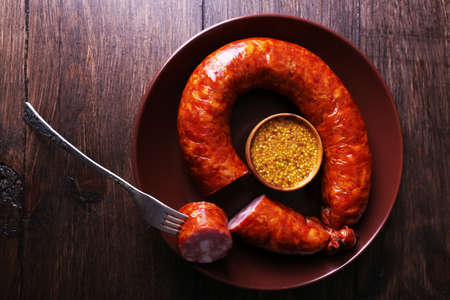 Smoked sausage with mustard on plate on wooden table backgroundの写真素材