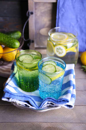 Fresh water with lemon and cucumber in glassware with napkin on wooden backgroundの写真素材