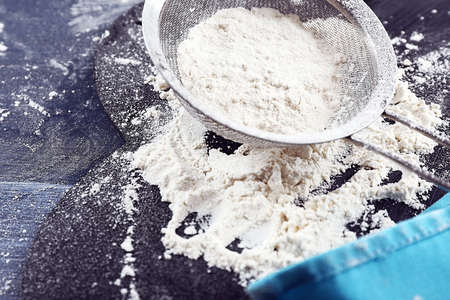 Sifting flour through sieve on wooden table, closeupの写真素材