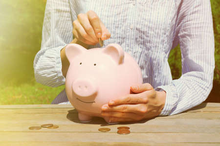Female hand putting coin into pink piggy bank, outdoorsの写真素材