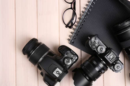 Modern cameras with glasses and notebook on wooden table, top viewの写真素材