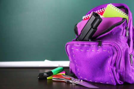 Gun in school backpack on wooden desk, on blackboard backgroundの写真素材