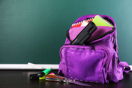 Gun in school backpack on wooden desk, on blackboard backgroundの写真素材