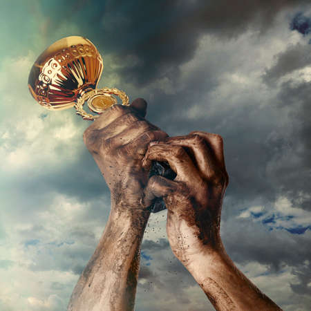 Gold cup in dirty hands on sky backgroundの写真素材