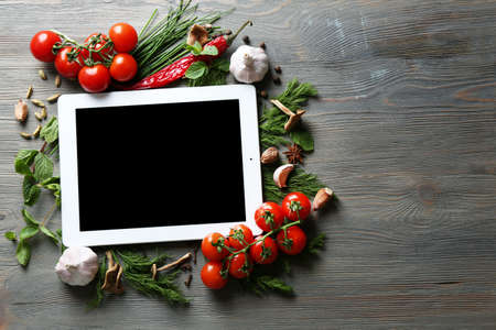Digital tablet with fresh herbs, tomatoes and spices on wooden backgroundの写真素材