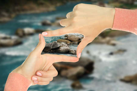 Woman holds hands in the shape of a frame on nature backgroundの写真素材