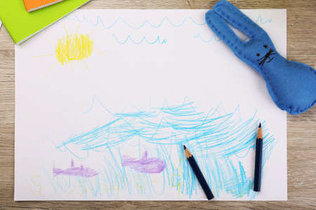 Kids drawing on white sheet of paper with crayons on wooden table, closeupの写真素材