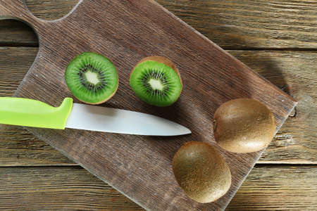 Juicy kiwi fruit with knife on cutting board on wooden backgroundの写真素材