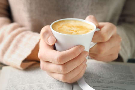 Woman holding cup of coffee and read the book, close upの写真素材
