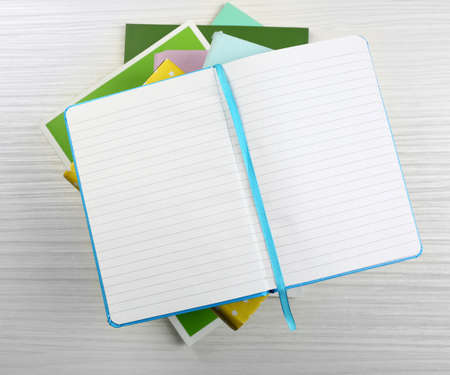 Notebook on top of pile of books and magazines on wooden backgroundの写真素材