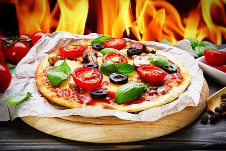 Tasty hot pizza with vegetables and basil on fire flame backgroundの写真素材
