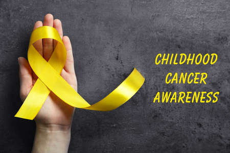 Hand holding yellow ribbon and text Childhood Cancer Awareness on dark backgroundの写真素材
