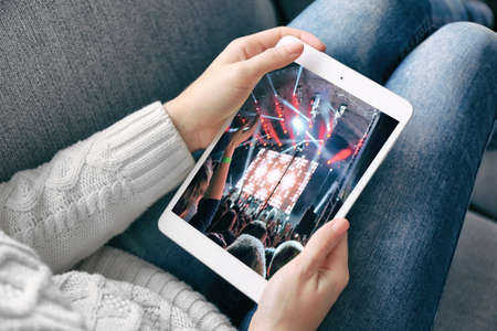 Female hand holding PC tablet on home interior background. Spotlight with laser rays on screenの写真素材