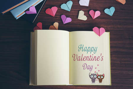 Opened notebook with text happy valentines day on page. Colorful origami hearts on wooden table.の写真素材