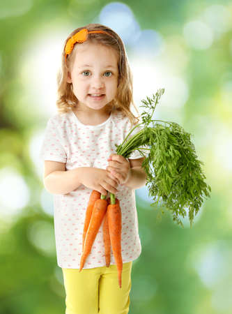 Cute little girl with carrots on blurred green background. Healthy food concept.の写真素材