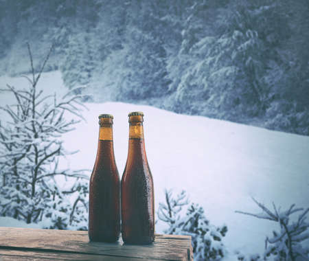 Glass bottles of beer on wooden table against winter nature background.の写真素材