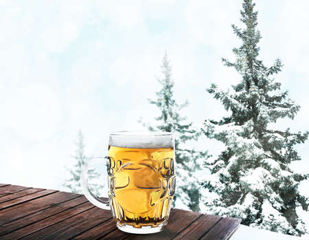 Glass of beer on wooden table against winter nature background.の写真素材