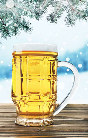 Glass of beer on wooden table against winter nature background.の写真素材