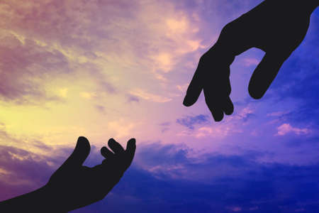 Silhouettes of father and child hands reaching to each other on sky background. Help and care concept.の写真素材