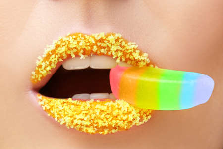Beautiful young woman with creative makeup holding marmalade in mouth, closeupの写真素材