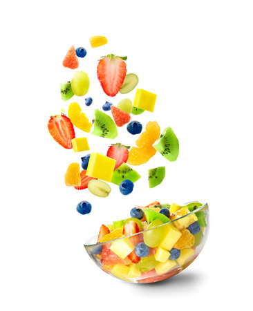 Sliced fruits falling into bowl with salad on white backgroundの写真素材