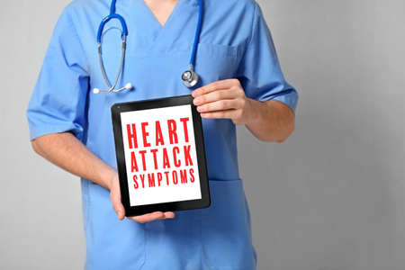 Cardiology and health care concept. Doctor's hands holding tablet with text HEART ATTACK SYMPTOMSの写真素材