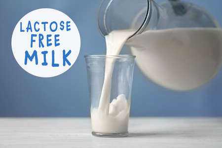Allergic food products concept. Pouring milk from jug into glass on blue backgroundの写真素材